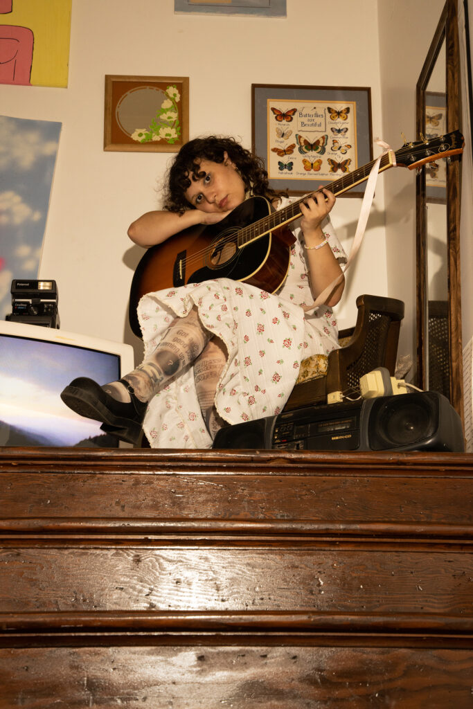Mik Sullivan sitting at the top of a staircase resting her head and arm on top of her guitar
